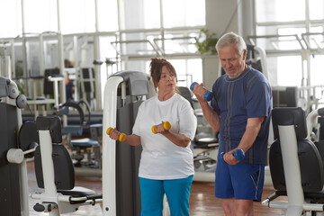 Fototapeta na wymiar Elderly couple exercising at gym. Senior people in gym lifting dumbbells. Older people healthy lifestyle.