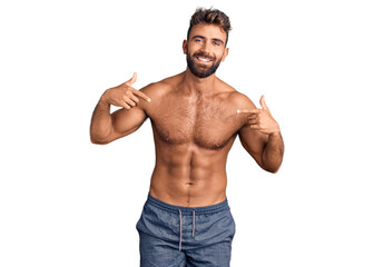 Young hispanic man wearing swimwear shirtless looking confident with smile on face, pointing...