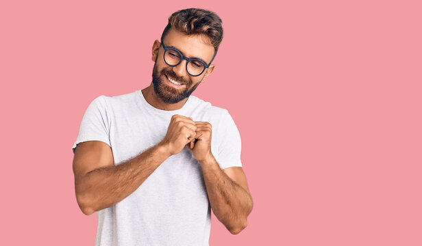 Young hispanic man wearing casual clothes and glasses laughing nervous and excited with hands on chin looking to the side