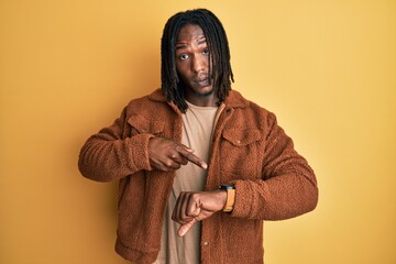 African american man with braids wearing brown retro jacket in hurry pointing to watch time,...