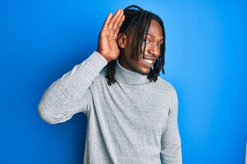 Fototapeta na wymiar African american man with braids wearing turtleneck sweater smiling with hand over ear listening an hearing to rumor or gossip. deafness concept.