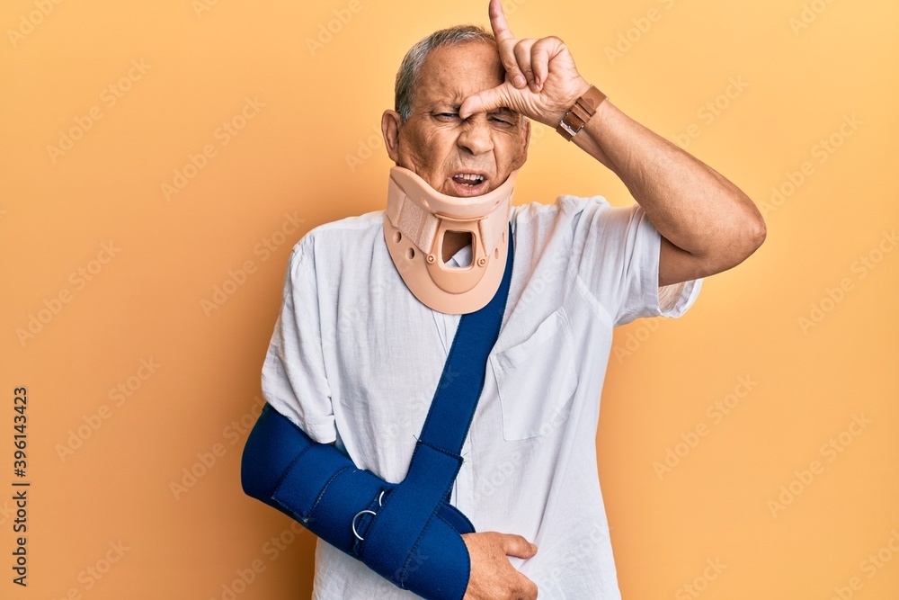 Sticker Handsome mature senior man wearing cervical collar and arm on sling making fun of people with fingers on forehead doing loser gesture mocking and insulting.