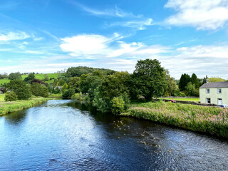 Fototapeta na wymiar Looking over the River Ribble, from the old stone bridge, with trees, houses and hills in the distance in, Sawley, Clitheroe, UK
