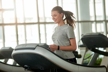 Young beautiful lady running on treadmill. Pretty smiling female person exercising at gym. Youth, sport, active way of life.