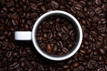 Detailed full frame top view of dark brown coffee beans. Outlines of white coffee mug in the middle.