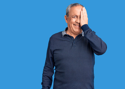 Senior handsome man wearing casual polo covering one eye with hand, confident smile on face and surprise emotion.
