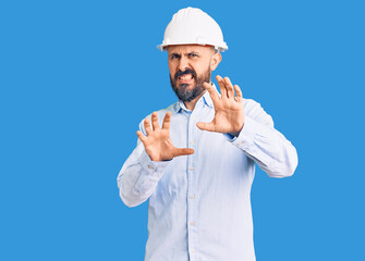 Young handsome man wearing architect hardhat disgusted expression, displeased and fearful doing disgust face because aversion reaction. with hands raised