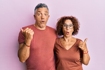 Obraz premium Beautiful middle age couple together wearing casual clothes surprised pointing with hand finger to the side, open mouth amazed expression.