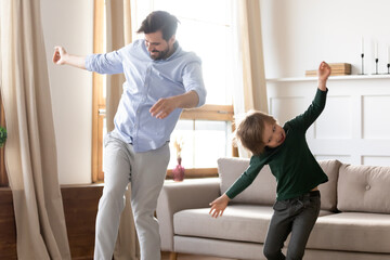 Fototapeta premium Overjoyed young Caucasian dad have fun enjoy weekend activity with excited small preschooler son. Happy single father dance jump with little boy child, play together at home. Entertainment concept.