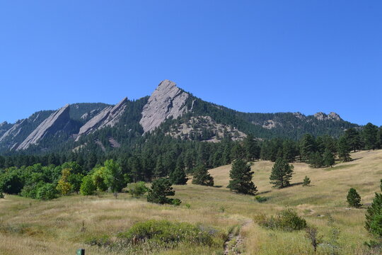 Mountain peak and ridge of the Flat Irons, with bright blue sky, pine trees and hiking trails in Boulder, Colorado.