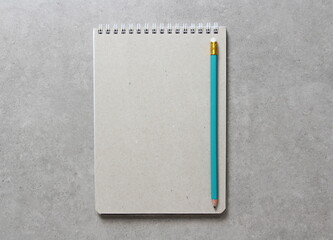 A spring notebook with a sheet of craft paper A5 with simple green graphite pencil on light grey concrete background. Concept of new idea, business plan and strategy. Empty space for text.