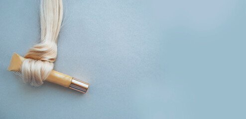 Care cosmetics in a tube wrapped in a lock of hair on a gray background with space for text. Banner.