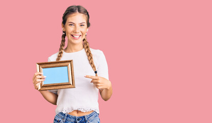 Beautiful caucasian woman with blonde hair holding empty frame smiling happy pointing with hand and finger