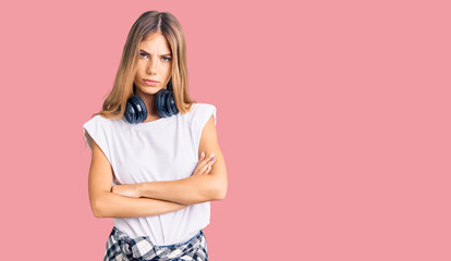 Obraz premium Beautiful caucasian woman with blonde hair listening to music wearing headphones skeptic and nervous, disapproving expression on face with crossed arms. negative person.