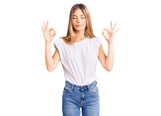Obraz na płótnie Canvas Beautiful caucasian woman with blonde hair wearing casual white tshirt relax and smiling with eyes closed doing meditation gesture with fingers. yoga concept.