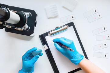 hands in blue medical gloves record the results of clinical trials. laboratory studies of drugs,...