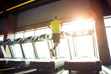 Cardio workout. Rear view of a mature athletic man in sportswear running on a treadmill in a gym,...