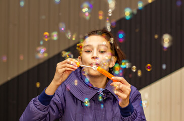 A young girl blows colorful bubbles in the park. Family recreation and entertainment concept.