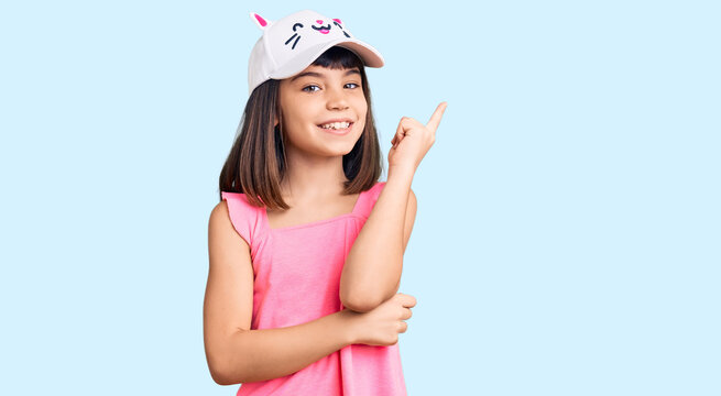 Young little girl with bang wearing funny kitty cap smiling happy pointing with hand and finger to the side