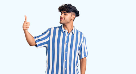 Young hispanic man wearing casual clothes looking proud, smiling doing thumbs up gesture to the side