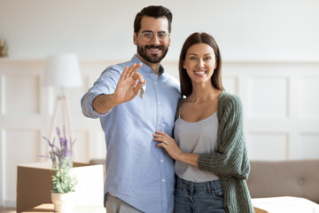 Portrait of happy Caucasian young couple renters show house keys buy first shared dwelling...