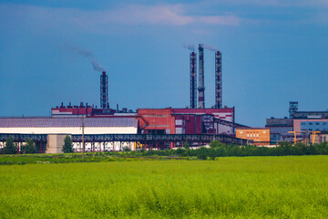 Fototapeta na wymiar Fumes of a mining plant against the sky and green grass.