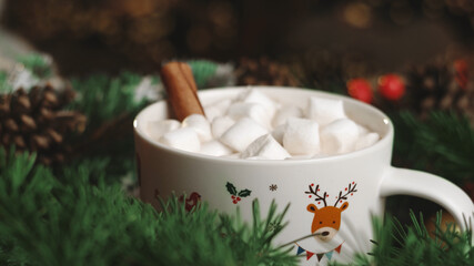 Hot cocoa with marshmallows, cinnamon in a white mug with patterns, surrounded by winter Christmas tree branches with berries and cones. The concept of a cozy holiday and New Year. Depth of field