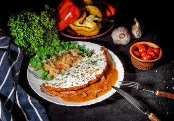 Potato pancakes with mushrooms sauce, sprinkled with herbs on dark background