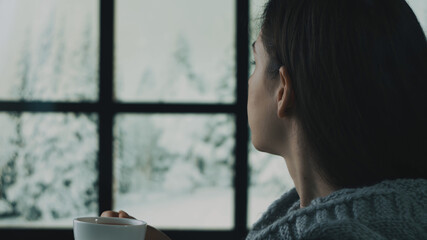 A beautiful girl is sitting in a cozy interior. Dreaming, thinking. Looking out the window. Festive interior with lights in the background. Winter day, cozy. Soft focus, depth of field