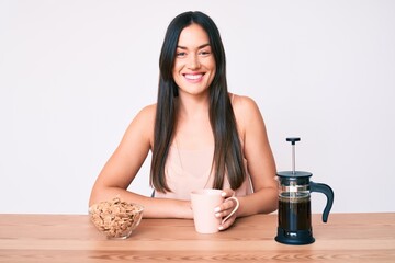 Young caucasian woman sitting at the table drinking coffee looking positive and happy standing and smiling with a confident smile showing teeth