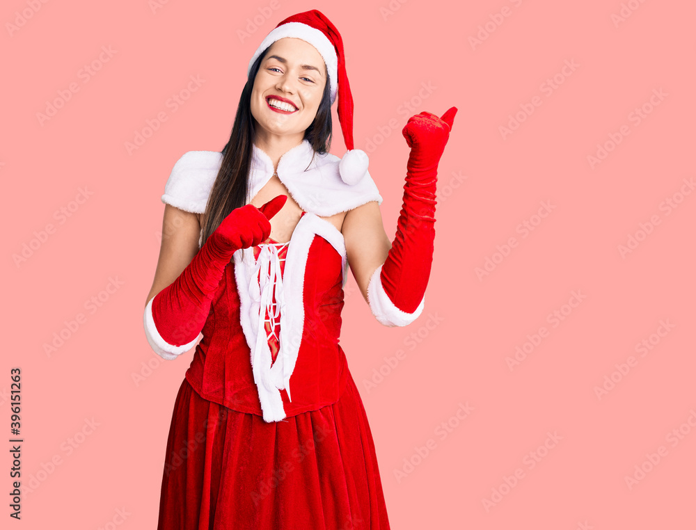 Sticker young beautiful caucasian woman wearing santa claus costume pointing to the back behind with hand an