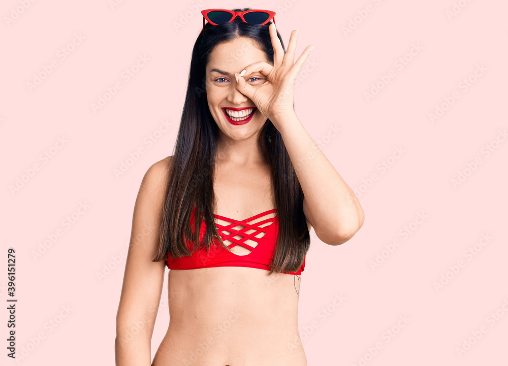 Poster young beautiful caucasian woman wearing bikini doing ok gesture with hand smiling, eye looking throu