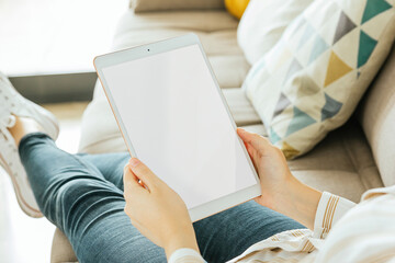 Tablet mockup held by a woman who is sitting on the couch. White screen