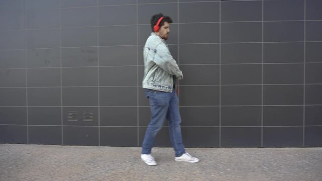 Man dancing while walking down the street, listening to music through a phone and red headphones