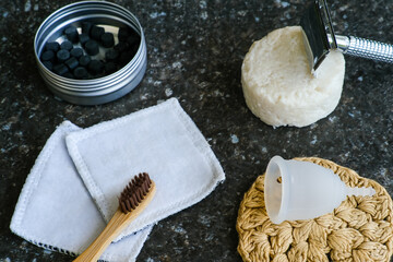 Natural cosmetic and bathroom accessories: bamboo toothbrush, solid toothpaste tablets, silicone menstrual cup, safety razor, crocheted cleansing pad. Zero waste sustainable plastic free lifestyle