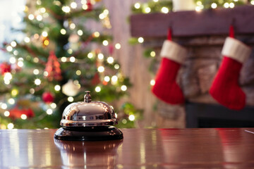 Christmas travel. Silver vintage bell on reception desk of guesthouse  and color shining garland on christmas tree on background. Hotel, restaurant. - 396152489