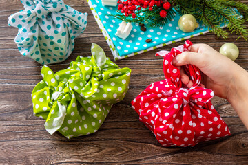 Child is holding Christmas gifts. New year and gift wrapping, zero waste furoshiki on wooden table.
