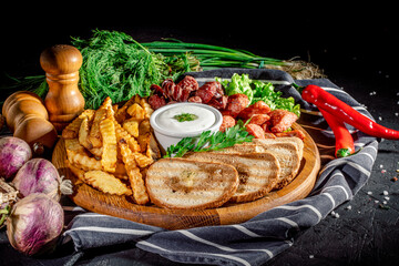Grilled sausages and french fries served with spicy sauce on the board on dark background. Appetizing beer snacks set