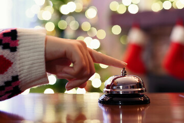 Christmas travel. Hand of guest ringing bell on reception desk of guesthouse and color shining...