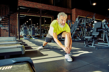 Warming up. Portrait of athletic middle aged man in sportswear stretching legs before training in a...
