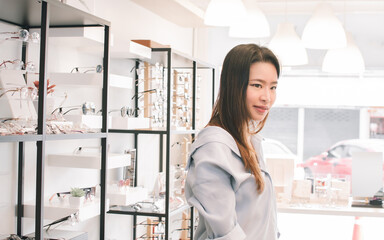 Asian young woman shopping eyeglasses in glasses store. Optical and Sales Promotion Concept.