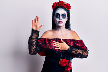 Young woman wearing mexican day of the dead makeup swearing with hand on chest and open palm, making a loyalty promise oath