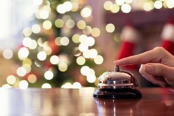 Hand of guest ringing reception bell on desk of guesthouse, hotel at christmas time. Color shining...