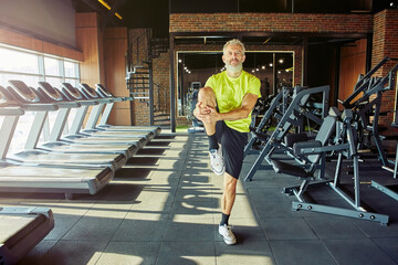 Fototapeta premium Stretching body. Portrait of athletic middle aged man in sportswear warming up before training in a gym or sport club