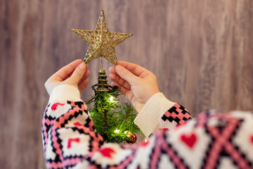 Woman decorating top of christmas tree with star at home. Cropped, close up