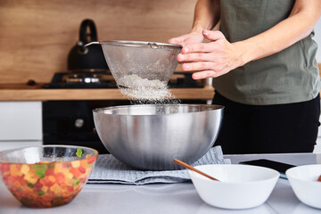 Woman in kitchen cooking a dough. Hands pour flour into a bowl