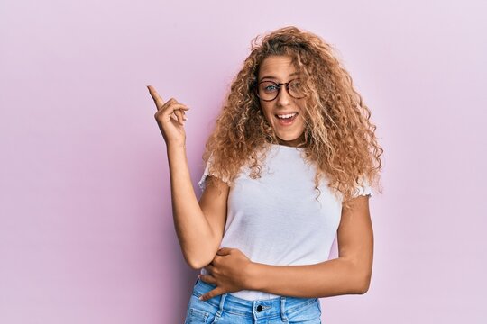 Beautiful caucasian teenager girl wearing white t-shirt over pink background with a big smile on face, pointing with hand and finger to the side looking at the camera.
