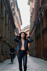 Portrait of beautiful young brunette woman in stylish black leather jacket, smiling on urban back