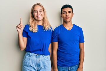 Young interracial couple wearing casual clothes showing and pointing up with finger number one while smiling confident and happy.