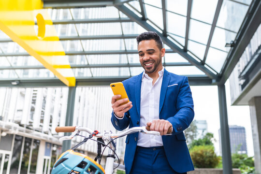 Young Businessman Using Cellphone While Walking Holding his Bike.